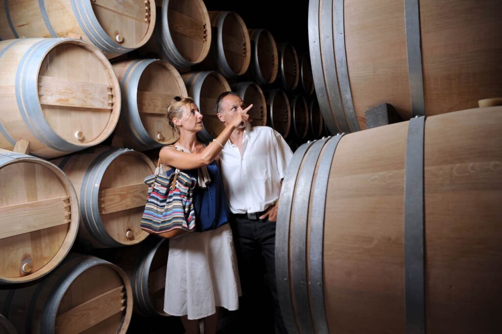A husband and wife in a wine cellar looking at oak barrels.