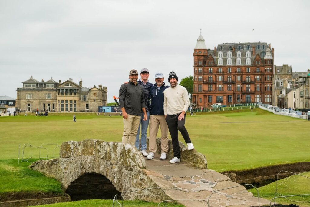 Four golfers pause for a photo on the Swilcan Bridge at St Andrews’ Old Course, framed by the iconic clubhouse and the Hamilton Grand behind them.